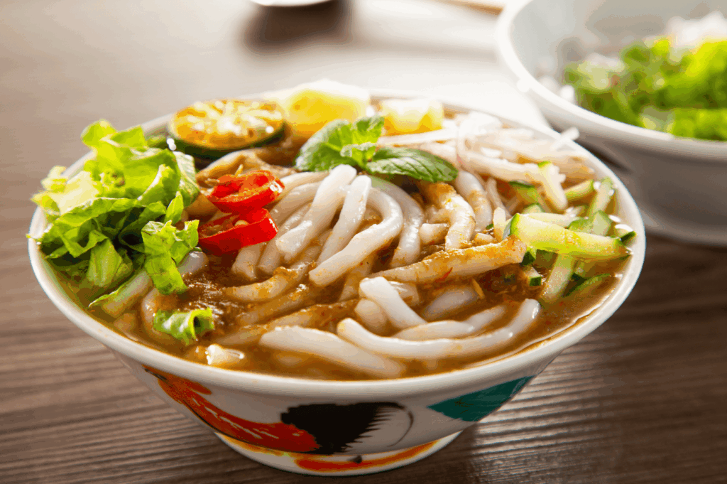 A regular bowl of assam laksa with rice noodles and thick bee hoon soaked in creamy laksa gravy made from coconut milk, evaporated milk, fresh coconut, and milk, cooked with laksa paste, blue ginger, dried shrimp, dried oysters, sambal, spices, sugar, lard, and garnish, then simmered to perfection. The spicy, flavourful broth is served with fish cake, fishcake, fried tofu puffs, tofu puffs, tau pok, bean sprouts, hard boiled egg, fresh prawns, prawns, cockles, blood cockles, chicken, and seafood, garnished with mint, cucumber, and lime. This tasty, savoury dish is a personal favourite found at laksa stalls like Asia Delight Laksa, Janggut Laksa, Yishun Laksa, Sungei Road Laksa, and Ng Chwee Seng, located near jalan besar, roxy square, and East Coast Road in Singapore. Whether in a small bowl or bowl with just a spoon or spoon, these stall opens at various opening hours in coffee shop and food centre settings, offering iconic katong laksa, Singapore Katong laksa, and the best laksa stalls with unforgettable taste, recipe, curry, and lemak richness—an essential eat for any food lover.