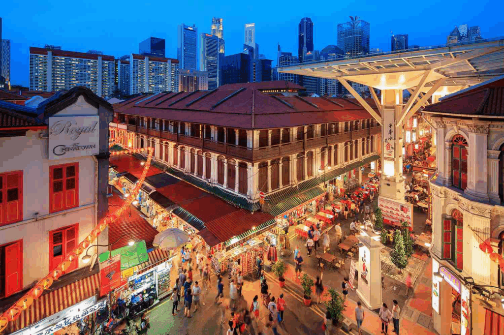 A lively evening street scene in Singapore’s Chinatown, near laksa stalls and food centres serving Singapore Katong laksa, katong laksa, and Singapore laksa. The bustling area, close to jalan besar, roxy square, and East Coast Road, is home to best laksa stalls like Asia Delight Laksa, Janggut Laksa, Yishun Laksa, Sungei Road Laksa, and Ng Chwee Seng. These coffee shop and stall locations offer laksa recipes featuring rice noodles, thick bee hoon, and noodles soaked in creamy laksa gravy made from coconut milk, evaporated milk, fresh coconut, and milk, cooked with laksa paste, blue ginger, dried shrimp, dried oysters, sambal, spices, sugar, lard, and garnish, then simmered to perfection. Toppings include fish cake, fishcake, fried tofu puffs, tofu puffs, tau pok, bean sprouts, hard boiled egg, fresh prawns, prawns, cockles, blood cockles, chicken, and seafood, served in a regular bowl or small bowl with just a spoon or spoon. This tasty, savoury, spicy dish is a personal favourite for its flavourful gravy, rich broth, and unforgettable taste. Whether exploring stall opens and opening hours or enjoying the soup soaked in lemak goodness, this food experience is a must-eat in Singapore.