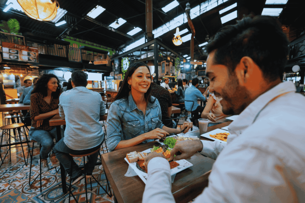 Indoor dining scene at one of Singapore's iconic hawker centres, where locals and tourists enjoy mouthwatering food like char kway teow with flat rice noodles, chinese sausage, and dark soy sauce, alongside hainanese chicken rice, nasi lemak with coconut milk, and other local dishes. The bustling food centre features hawker stalls and street food vendors serving stir fried noodles, satay, and malay dishes in a vibrant setting near the central business district and Singapore River. Capturing the real life hawker culture of southeast Asia, this must visit spot—possibly Maxwell Food Centre, Lau Pa Sat, or Airport Road Food Centre—offers great food, drinks like teh tarik and coffee, and sweet treats like shaved ice. A short walk from Orchard Road or Chinatown, this open air food court atmosphere reflects singapore's hawker centers and hidden gems praised by Anthony Bourdain. Perfect for a blog post or travel tips guide on local cuisine, food stalls, and public transport access across the city and surrounding islands.