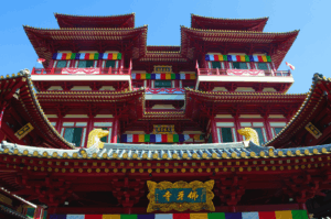 Buddha Tooth Relic Temple in Singapore’s Chinatown, a majestic Tang-style structure with red-and-gold tiered roofs, prayer flags, and ornate balconies—symbolizing the spiritual heart of tradition amid the district’s vibrant cultural evolution.