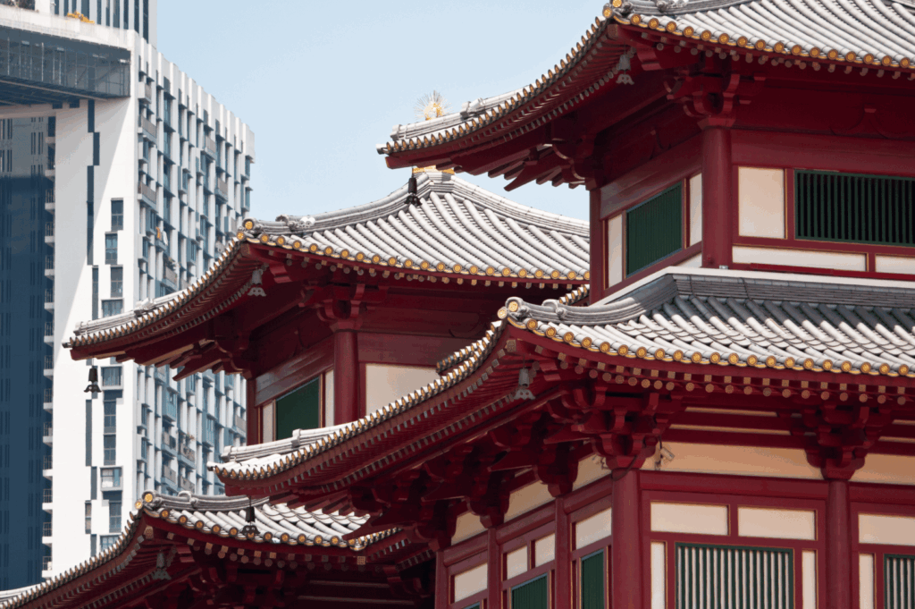 Close-up of ornate temple rooflines in Singapore’s Chinatown, with red pillars, upturned eaves, and intricate detailing—framed against a modern high-rise in the background, this scene captures the city’s layered dialogue between ancient craftsmanship and contemporary urban design.