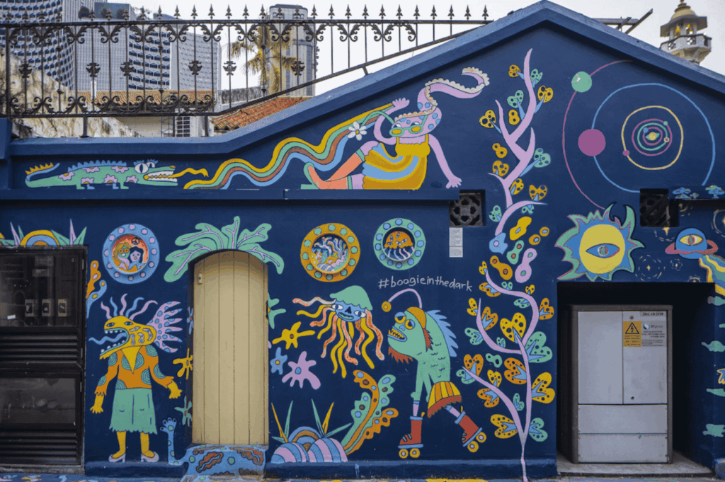 Whimsical cosmic‑themed mural painted on the exterior wall of a modern city building, part of the vibrant Singapore art scene where street art, urban art, and graffiti by local and international artists transform public spaces into open‑air art exhibitions. This imaginative visual arts work—featuring surreal creatures, abstract shapes, and cosmic motifs—reflects art forms from fine arts to performing arts, much like pieces at the Singapore Art Museum, National Gallery Singapore, and during the Singapore Biennale. Found near Victoria Street, Little India, and main streets lined with boutique shops, shops, and streets in neighbourhood hubs such as Haji Lane, Clive Street, Kerbau Road, Rowell Road, Ann Siang Hill, Tiong Bahru, and Chinatown, it embodies the multicultural society of Singapore—a young nation in the Asia Pacific region and Southeast Asia. Influences from Chinese immigrants, India, China, and Asia merge with art deco and modern way styles, echoing works by Yip Yew Chong, Ernest Zacharevic, and Novena Angela, who have helped develop art in Singapore. The scene connects history, culture, life, music, food, and ideas with important role heritage supported by the National Heritage Board, Nanyang Academy, and Art SG, celebrating emerging artists, the new generation, and international artists. From early exhibitions to contemporary scene highlights in the central business district, main road corridors, and events inspired by Crazy Rich Asians, this collection of sculptures, art, and inspired works cements Singapore’s place in the world of creativity.