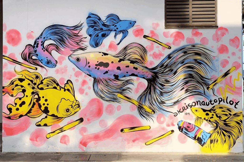 Vibrant mural painted on a wall in the modern city of Singapore, featuring colorful stylized fish swimming among abstract pink shapes and yellow cylinders, with a paint tube spilling vivid colors—an imaginative example of street art, urban art, and singapore street art within the Singapore art scene. Found near public spaces, main streets, and boutique shops in neighbourhood hubs like Victoria Street, Little India, Haji Lane, Clive Street, Kerbau Road, Rowell Road, Ann Siang Hill, Tiong Bahru, and Chinatown, it reflects the multicultural society of a young nation in the Asia Pacific region and Southeast Asia. Influences from Chinese immigrants, India, China, and Asia merge traditional and art deco ideas with a modern way of storytelling, similar to works by local and international artists—including Yip Yew Chong, Ernest Zacharevic, and Novena Angela—who have helped develop art in Singapore. Supported by the National Heritage Board, Nanyang Academy, and Art SG, the piece celebrates emerging artists, the new generation, and international artists through art exhibitions, the Singapore Biennale, and collection highlights of sculptures, fine arts, performing arts, music, food, and life. From early exhibitions to today’s contemporary scene, this inspired work plays an important role in connecting history, culture, shops, streets, main road corridors, local events, and even pop culture moments like Crazy Rich Asians, cementing Singapore’s place in the world of creativity and visual arts.