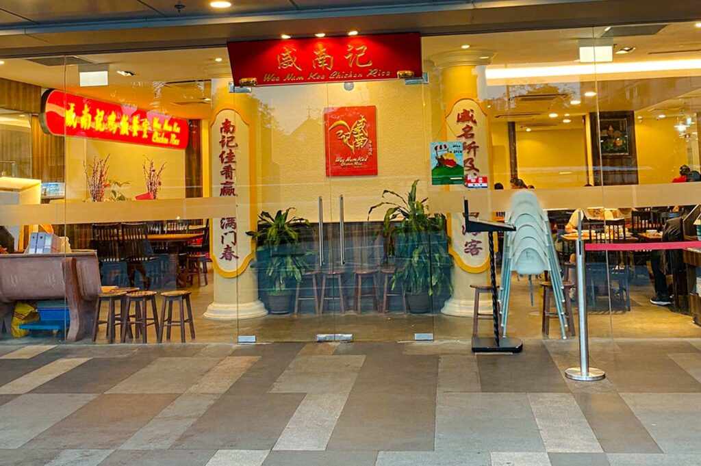 Glass‑front entrance of Wee Nam Kee Chicken Rice restaurant in Singapore, displaying traditional red and gold signage, warm interior lighting, and classic décor associated with authentic Hainanese chicken rice dining.
