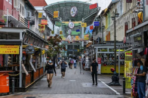 The arched, modern entrance to Pagoda Street in Singapore's Chinatown, flanked by colorful traditional shophouses, with people walking along the pedestrian walkway.