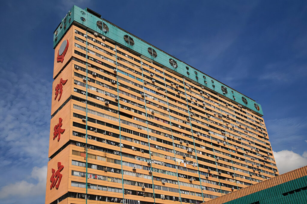 The massive, high-rise People's Park Complex in Chinatown, featuring its distinctive orange facade with Chinese characters and a teal roofline, viewed against a bright blue sky.