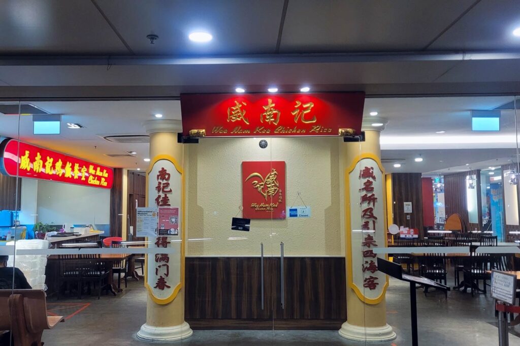 Wee Nam Kee Chicken Rice restaurant entrance with bright red signage, Chinese calligraphy panels, and a view of neatly arranged dining tables inside.