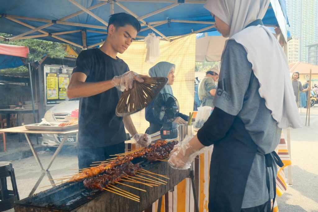 Exploring Kampong Glam Heritage : Smoke rising as a street vendor fans the flames beneath sizzling satay.