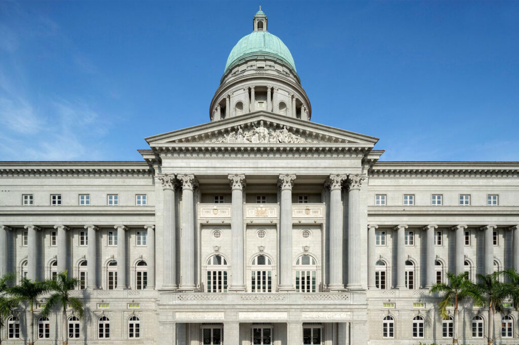 A direct, symmetrical front view of the National Gallery Singapore building, highlighting its grand colonial architecture, imposing columns, and pale green dome.
