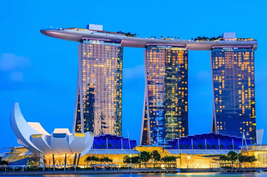 The iconic Marina Bay Sands hotel complex at dusk, featuring its three towers topped by a boat-shaped Skypark, with the lotus-shaped ArtScience Museum in the foreground.