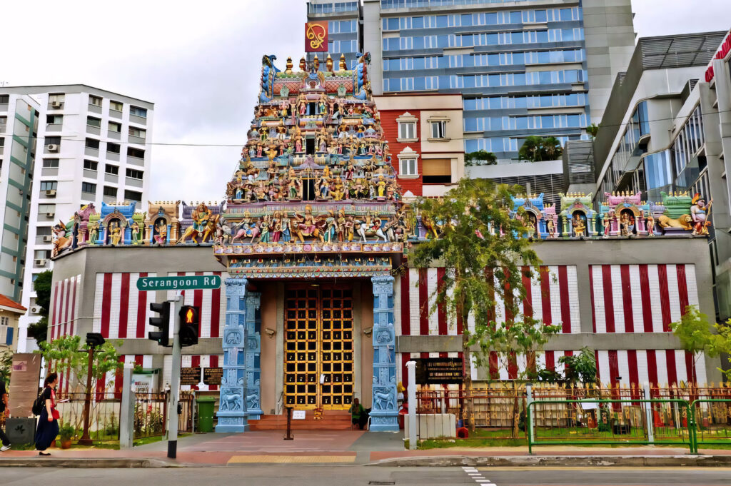 Exterior view of the ornate and brightly colored gopuram (tower entrance) of the Sri Veeramakaliamman Temple on Serangoon Road, set against modern high-rise buildings.