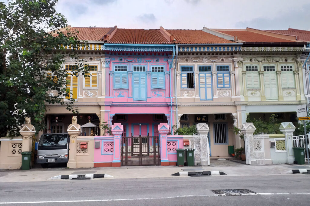 A row of meticulously restored, brightly painted Peranakan shophouses in the Joo Chiat/Katong area of Singapore, notably featuring a striking pink and blue facade.
