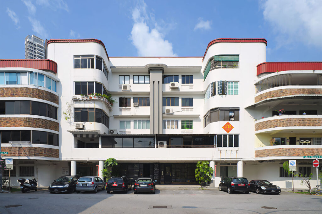 Wide street view of a prominent white, pre-war apartment block in Tiong Bahru, Singapore (likely Block 78), showcasing the unique Streamline Moderne architecture with curved corners and horizontal lines.