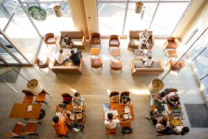 This is a high-angle, overhead shot of the interior of a brightly lit Starbucks coffee shop in Nakhon Pathom, Thailand, featuring various seating arrangements and patrons.