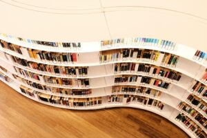 This image captures a uniquely designed white bookshelf, filled with various books, that curves in a distinct wave-like pattern across the frame.