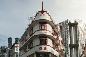 This image features a distinctive white Art Deco-style building with curved balconies, red shutters, and the year "1939" displayed near its peak. Behind this heritage structure, towering modern skyscrapers rise into the sky, creating a striking visual contrast between the city's historical architecture and contemporary urban development.