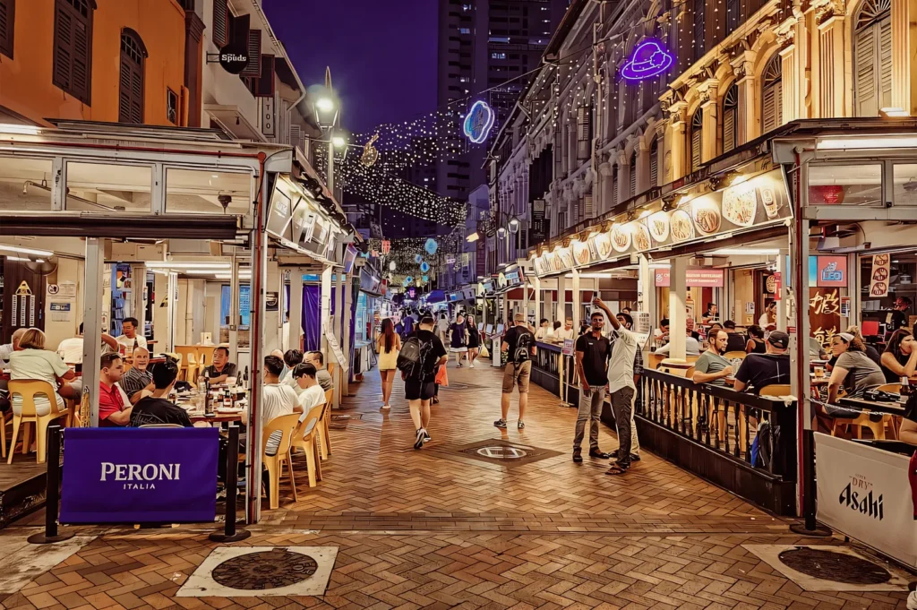Wide-angle street-level night shot of Pagoda Street near Chinatown MRT, featuring busy outdoor restaurants, diners enjoying Chinatown MRT food, illuminated shophouses, and a lively pedestrian dining atmosphere.