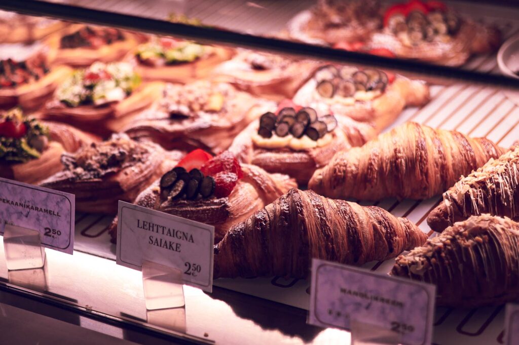 Bakery display case with fresh croissants, caramel pecan danish, almond cream pastries, and fruit‑topped treats.