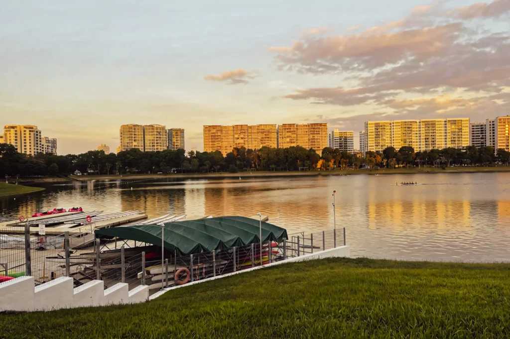 Golden hour view of Bedok Reservoir featuring boat rental docks, calm water, and high‑rise residential buildings reflecting the sunset.