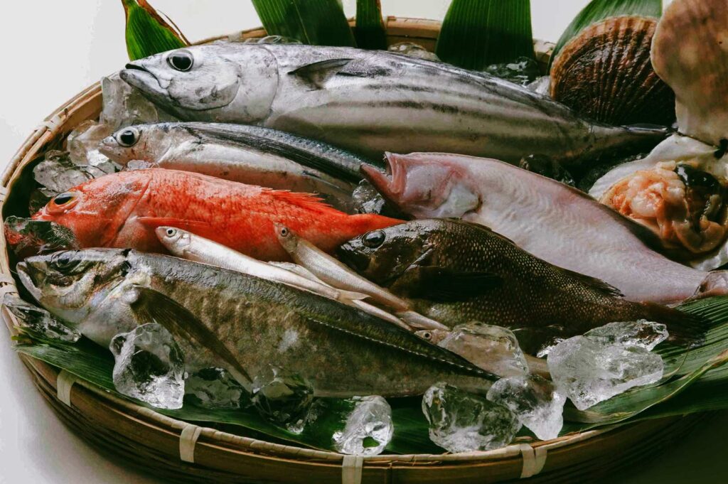 A basket of assorted fresh seafood on ice, including whole fish, shellfish, and seasonal catches, prepared for a high‑end sushi omakase menu.