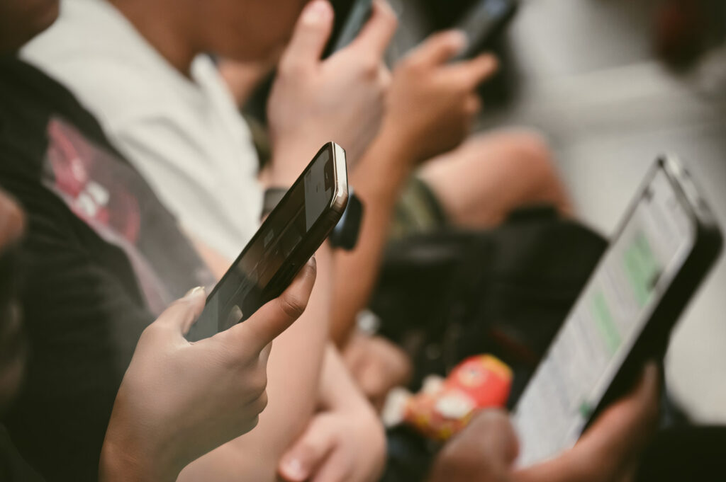 A close-up of several hands holding smartphones, with screens displaying messages and apps while seated closely together.