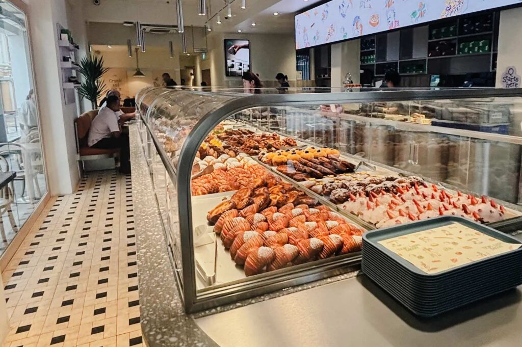 Modern bakery with a long glass display case showcasing assorted pastries, croissants, and desserts, set within a stylish café interior.