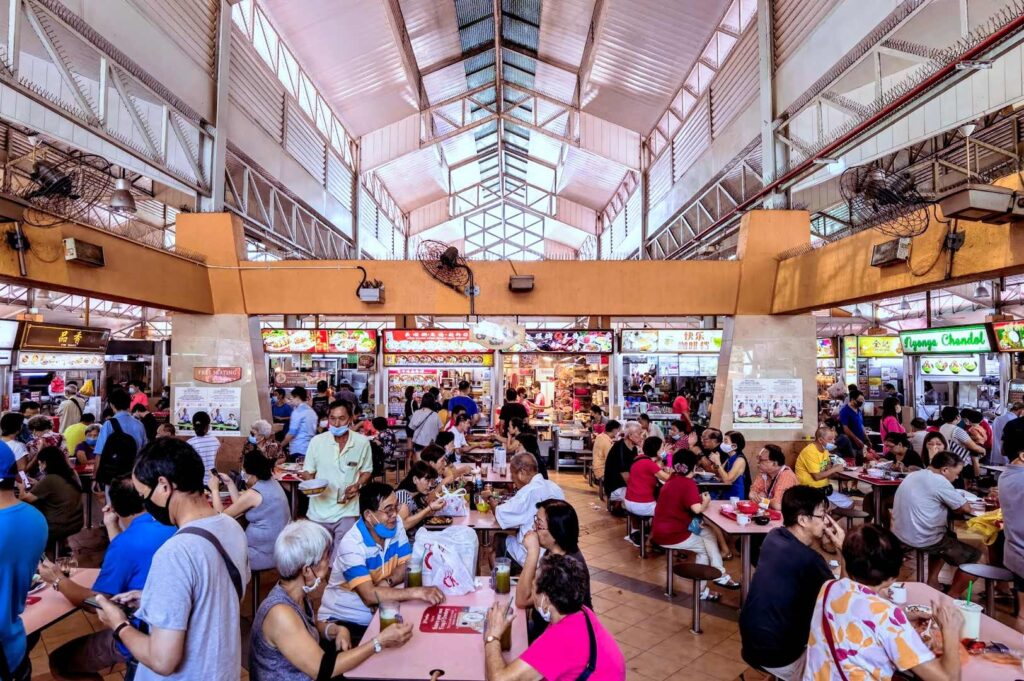Front facade of 51 Old Airport Road Food Centre & Shopping Mall, featuring a bright yellow sign, geometric building patterns, and a clear blue sky.