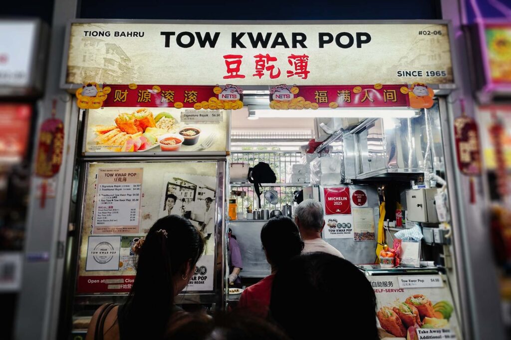 Tow Kwar Pop stall at Tiong Bahru Market featuring a lighted signboard, displayed menu items, and customers lining up to order the traditional beancurd dish.