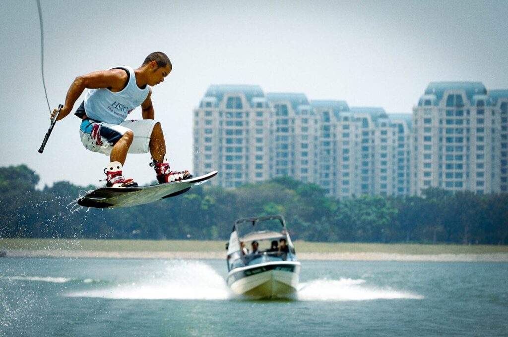 Wakeboarder performing a jump over Bedok Reservoir with a speedboat behind.
