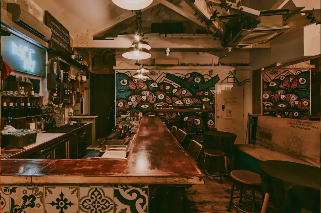 Eye-level wide shot of a rustic industrial-style bar in Singapore featuring a long wooden counter, patterned tiles, wall art, and warm ambient lighting.