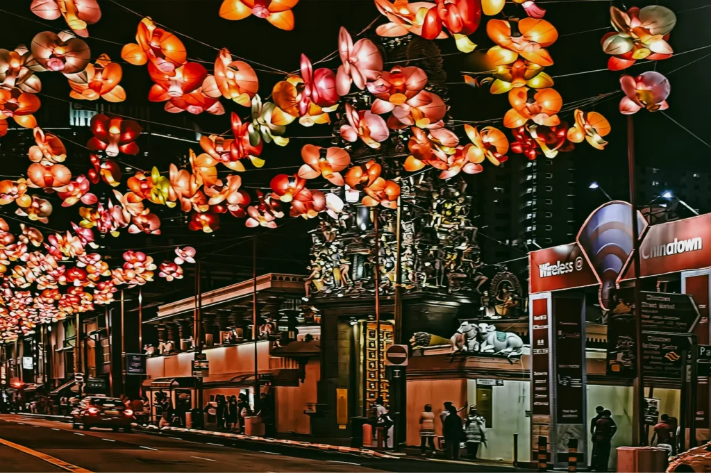 Wide-angle street-level view of glowing flower lanterns lighting up a Chinatown street in Singapore during the Mid-Autumn Festival.