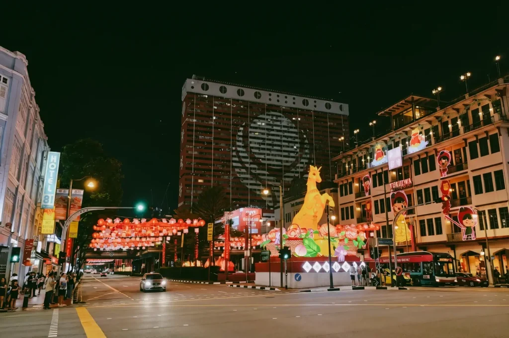 Wide-angle night shot of Chinatown in Singapore decorated for Chinese New Year, featuring red lanterns, festive arches, zodiac sculptures, and illuminated shophouses along a busy street.