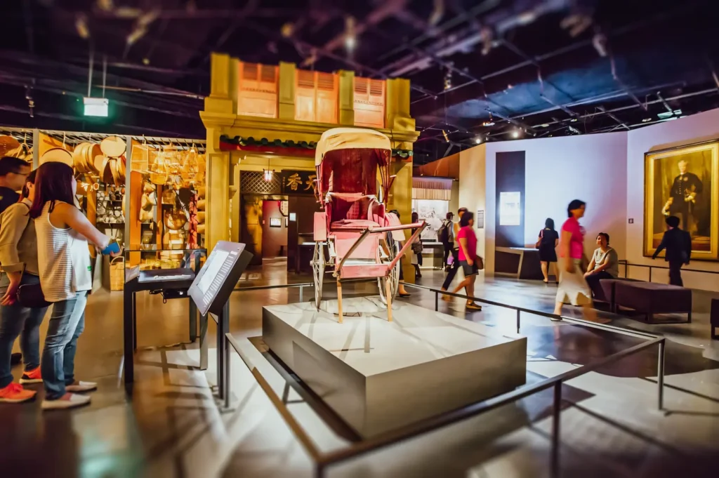 Wide‑angle interior shot of a museum gallery with a historical carriage displayed at the center, surrounded by exhibits, informational panels, and visitors, showcasing cultural attractions and heritage exhibitions.
