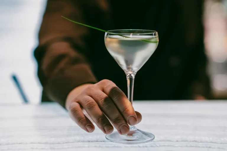 Eye-level close-up of a bartender placing a classic martini cocktail with green garnish on a marble bar at a luxury Singapore cocktail bar.