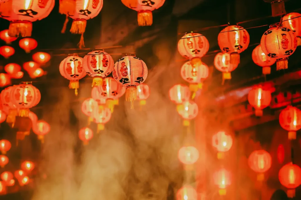 Low‑angle shot of glowing red Chinese lanterns in rows, festive Lunar New Year decor against hazy night sky.