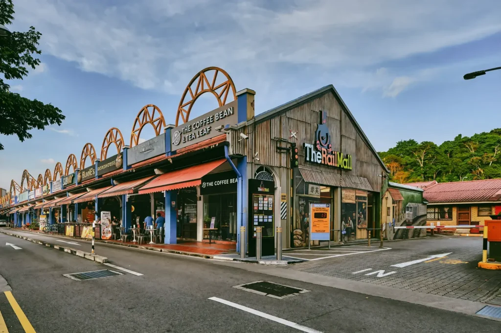 Wide-angle street-level shot of Rail Mall in Bukit Timah, Singapore, showing The Coffee Bean & Tea Leaf and other heritage-style shopfronts along a quiet road under a blue sky.