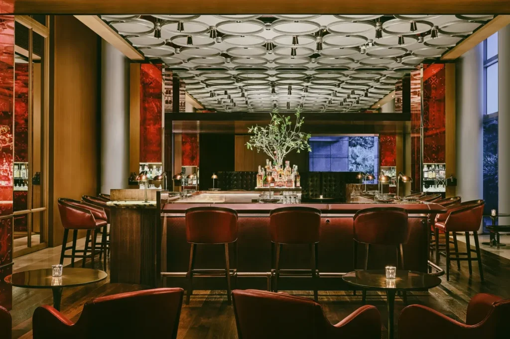 Symmetrical eye-level shot of an upscale hotel bar in Singapore with a central marble counter, designer ceiling lights, and elegant bar seating.