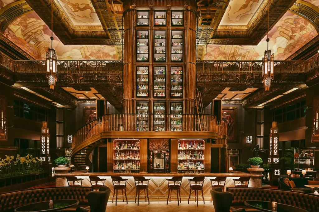 Low-angle wide shot of a luxurious Art Deco bar in Singapore with a towering back bar, ornate ceiling murals, and elegant seating.