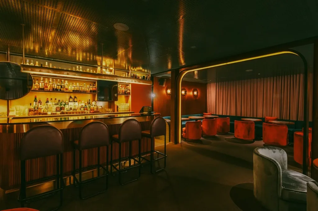 Wide-angle interior shot of an intimate speakeasy-style bar in Singapore with warm amber lighting, plush seating, and a fully stocked back bar.