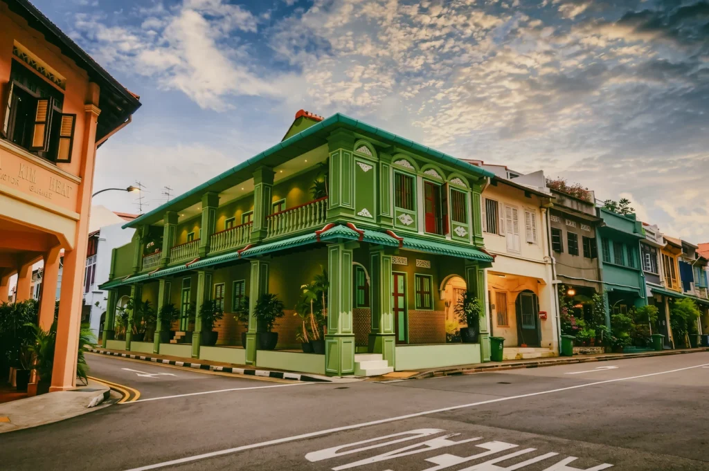 Low-angle wide shot of a green pre-war shophouse at a quiet Singapore neighbourhood corner, highlighting heritage architecture and pastel details