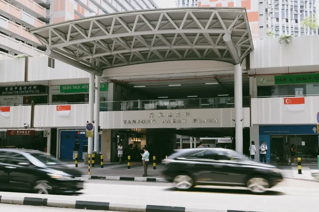 Front-facing street-level shot of Tanjong Pagar Plaza with passing traffic, capturing a community hub that connects everyday local life with Singapore’s central business district
