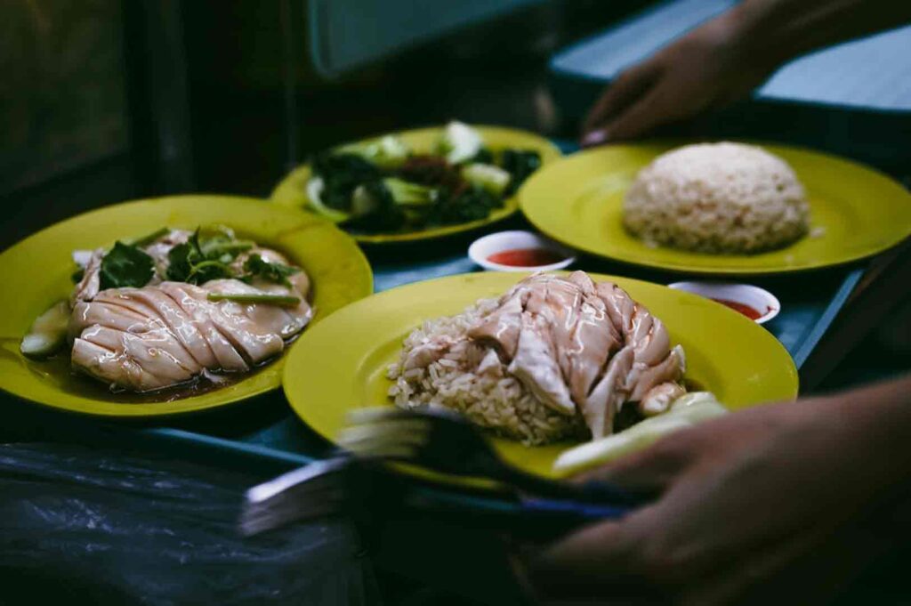 Close-up overhead shot of Hainanese chicken rice served on green plates at a Singapore hawker centre, representing local food culture and shared family dining.