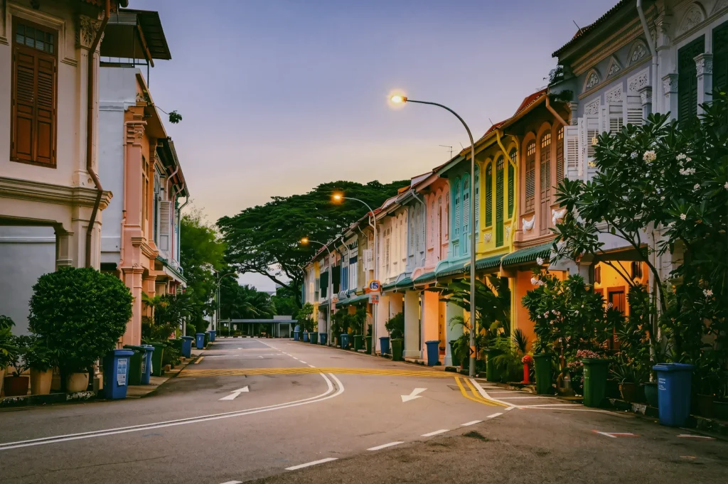 Eye-level wide shot of a pastel-coloured Singapore shophouse street, showcasing calm residential life and neighbourhood charm