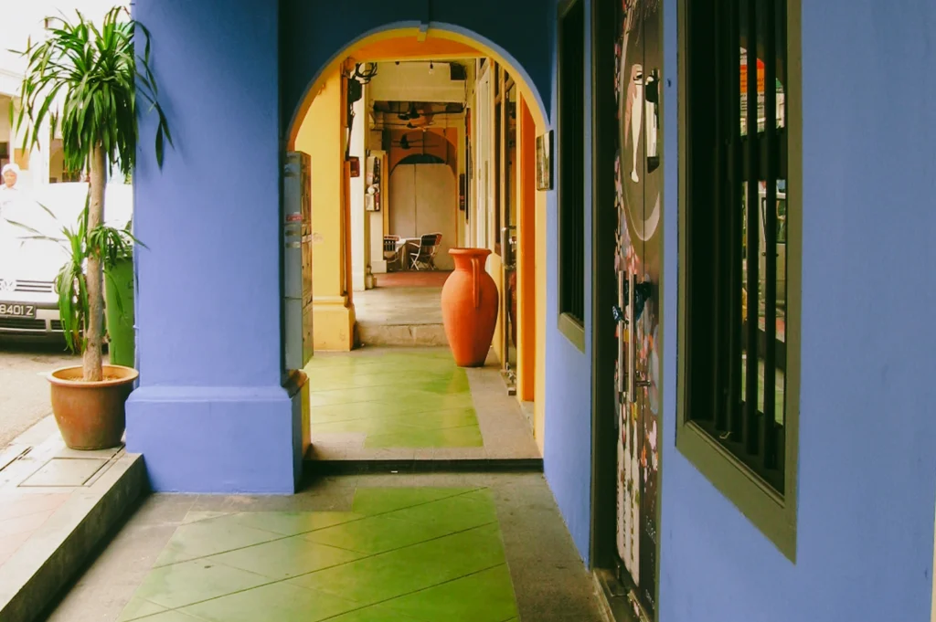 Leading-line interior shot of traditional five-foot way corridor in a Peranakan shophouse, with arched doorway, colorful walls, and tiled flooring reflecting preserved cultural design in Joo Chiat.