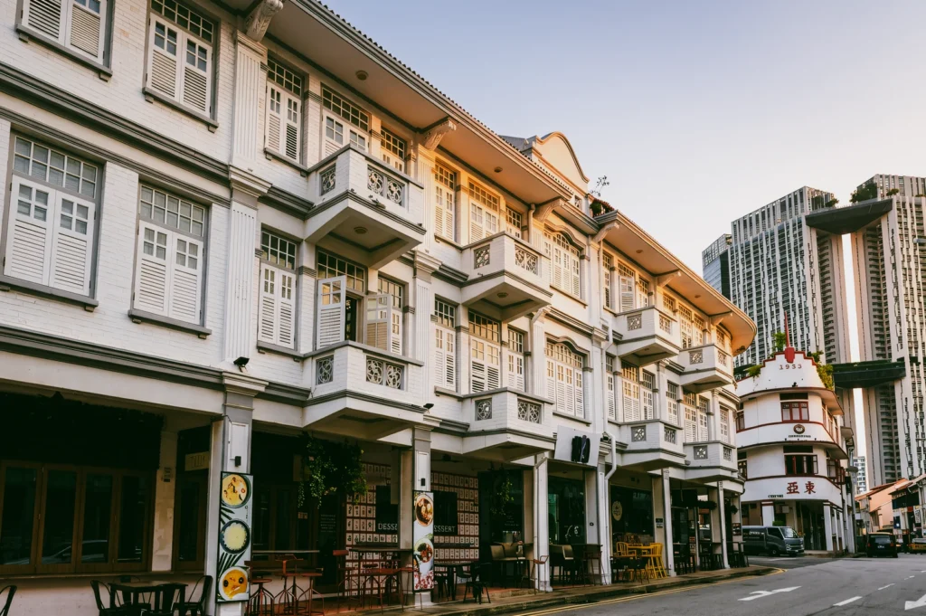 Street-level angled perspective of conserved Singapore shophouses with ornate shutters and balconies, warm morning sunlight illuminating heritage architecture in Chinatown district