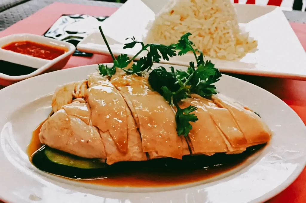 Close-up overhead angle of Hainanese chicken rice served with soy sauce and chili dip, highlighting a signature Singapore Chinese dish that represents culinary heritage and modern local cuisine