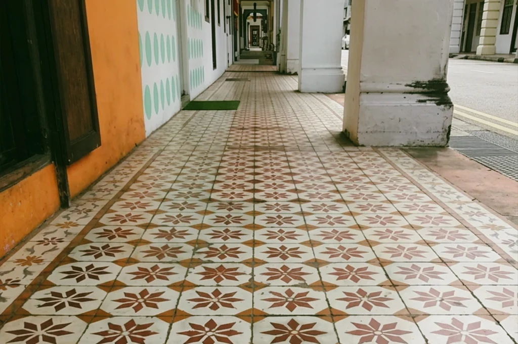 Low-angle close-up shot of geometric ceramic tiles along a Singapore five-foot way, worn smooth by decades of daily footsteps