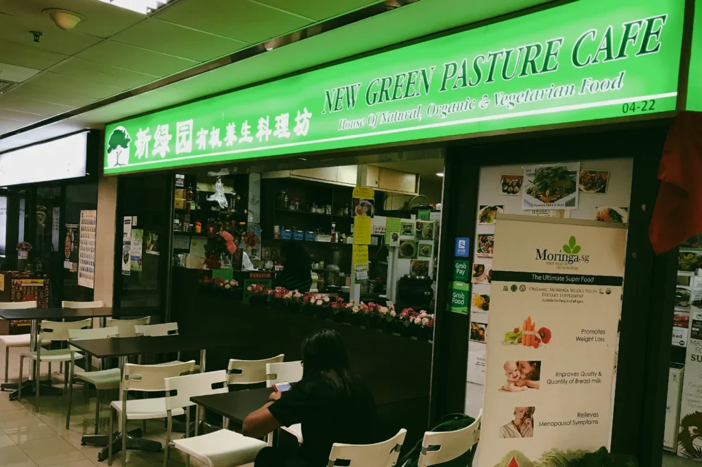 Slight angle eye-level shot of New Green Pasture Cafe storefront at Fortune Centre, highlighting organic vegetarian restaurant with indoor seating area