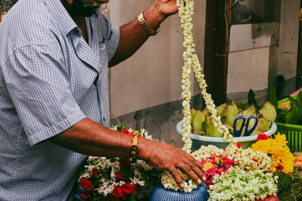 Close-up side-angle shot of flower garland maker arranging fresh jasmine and marigold strands, capturing traditional craft and Little India street culture in Singapore