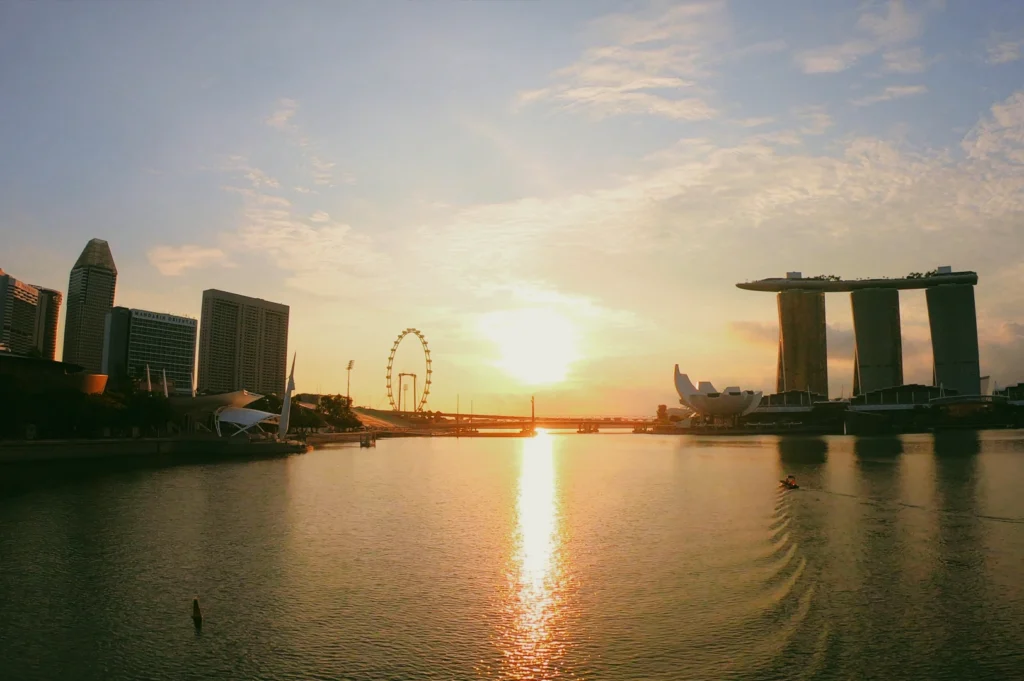 Wide panoramic shot of the Singapore River at sunrise, with Marina Bay skyline reflected in calm water during golden hour